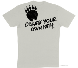 A light beige t-shirt back image containing a graphic of a grizzly bear paw on the top of the left side of the shirt with the slogan "Create Your Own Path Wilden Trail" underneath at an angle.