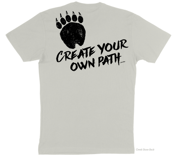 A light beige t-shirt back image containing a graphic of a grizzly bear paw on the top of the left side of the shirt with the slogan "Create Your Own Path Wilden Trail" underneath at an angle.