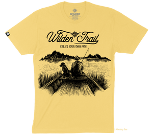 Light yellow t-shirt with black graphic design of a man and lab fishing in a boat on a lake with mountains in the background. 'Wilden Trail Create Your Own Path text at the top of the design.