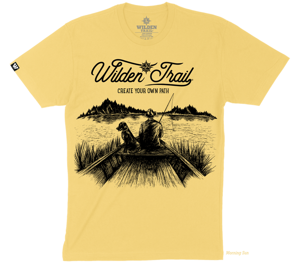 Light yellow t-shirt with black graphic design of a man and lab fishing in a boat on a lake with mountains in the background. 'Wilden Trail Create Your Own Path text at the top of the design.