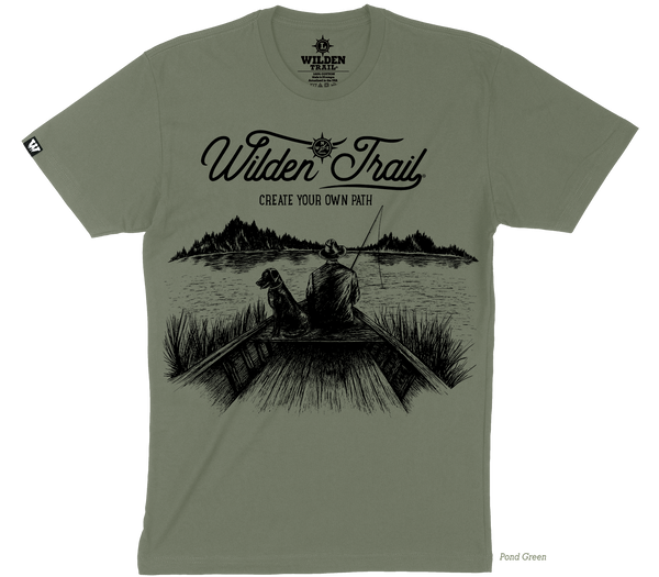 Army green t-shirt with black graphic design of a man and lab fishing in a boat on a lake with mountains in the background. 'Wilden Trail Create Your Own Path text at the top of the design.