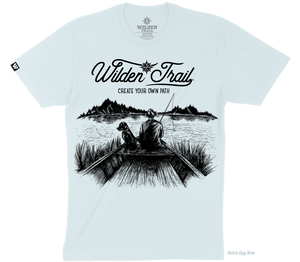Light blue t-shirt with black graphic design of a man and lab fishing in a boat on a lake with mountains in the background. 'Wilden Trail Create Your Own Path text at the top of the design.