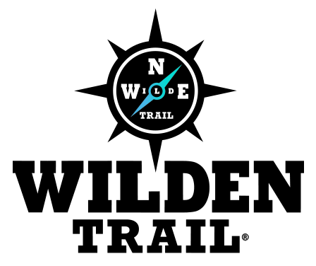 This is the Wilden Trail logo. It features a compass at the top with a light blue directional face, with the words “Wilden Trail” positioned beneath it. A registration mark appears in the lower right corner of the logo.